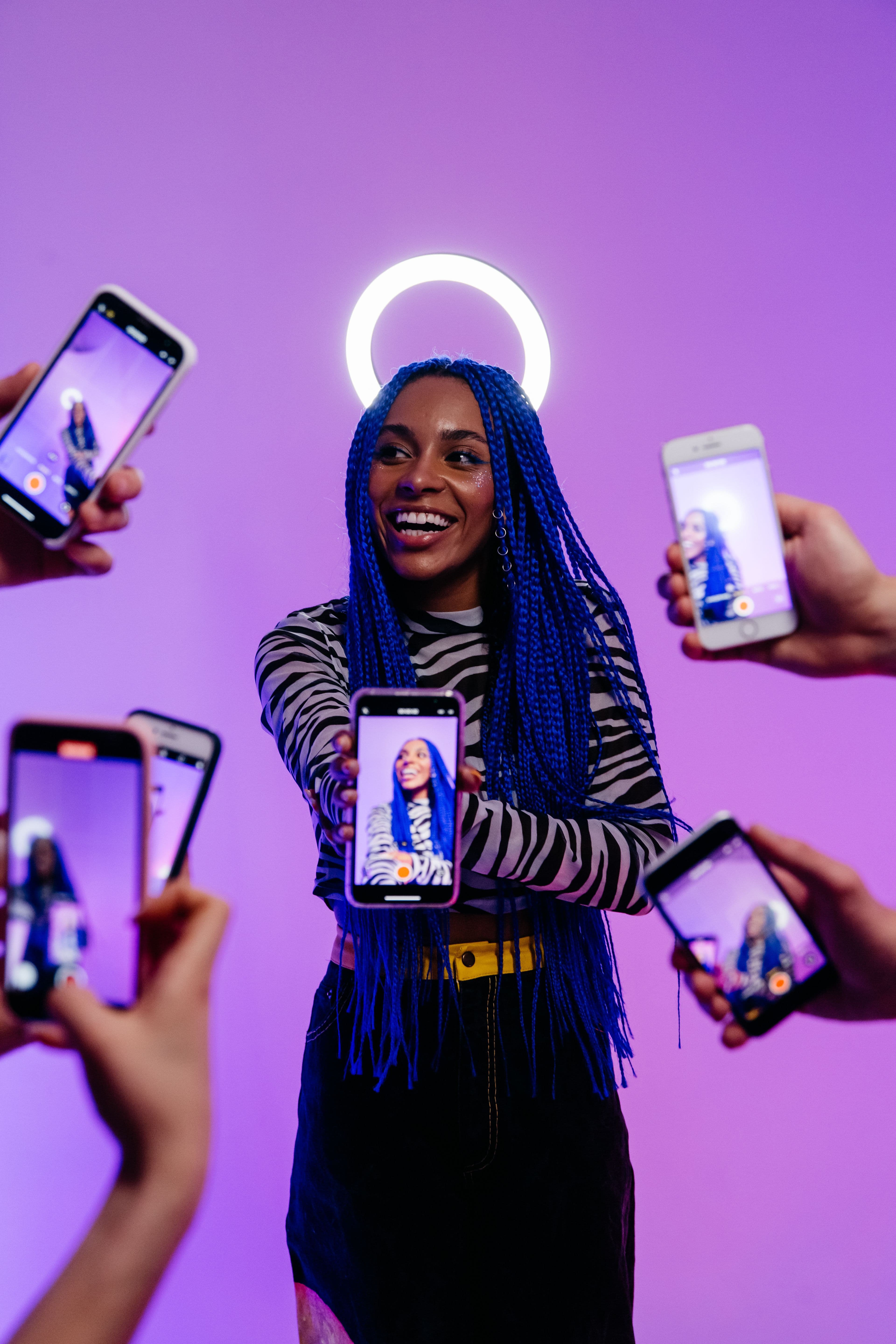 A creator holding out her phone, surrounded by hands filming her under a ring light